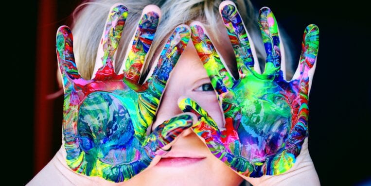 child looks through hands covered in finger paint