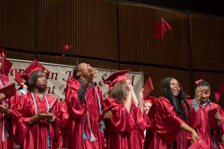Several students stand onstage in red graduation robes
